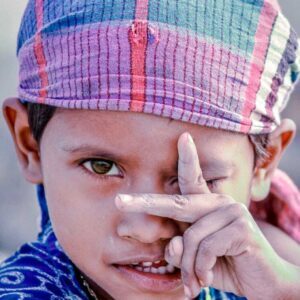 Playful young child peeking through fingers wearing colorful knit cap